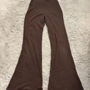 Bruna ribbade bootcut byxor - Snygga bruna byxor med ribbad struktur och bootcut-modell. Byxorna har en skön passform och är perfekta för dig som gillar en trendig och avslappnad stil. Materialet känns mjukt och stretchigt, vilket gör dem bekväma hela dagen.