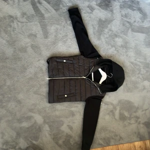 Svart pufferjacka med huva från H&M - Helt ny cardigan från H&M, bara testad. Jag har sytt fast en moncler logga  loggan var från en tshirt klippte bort den från thsirten sydde fast den på cardigan ist  för att ge den en personlig touch. Tyvärr lite för stor för mig, så jag säljer den vidare.