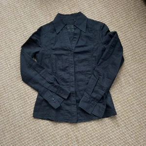 Svart skjorta från Esprit Collection - Klassisk svart skjorta från Esprit Collection med lång ärm och knappar framtill. Skjortan har en figurnära passform och är tillverkad i ett mjukt bomullstyg. Storlek 32k