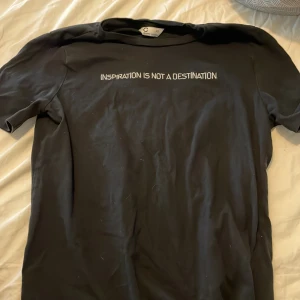 Svart t-shirt med texttryck XS - Svart t-shirt från C i ekologisk bomull med vit text på bröstet: 'Inspiration is not a destination'. Klassisk rund hals och korta ärmar, perfekt för en chill och stilren look.