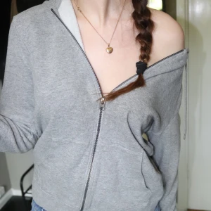 Grå hoodie med dragkedja och huva - Grå hoodie med dragkedja framtill och huva med snörning. Tröjan har en loose passform och långa ärmar. 
