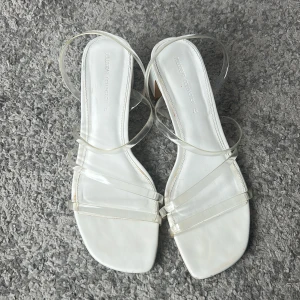 Vita sandaler med klack från Pull & Bear - Snygga vita sandaler från Pull & Bear med transparenta remmar och fyrkantig tå. Skorna har en låg klack på ca 5 cm och stilren design som passar perfekt till sommarens outfits. Köpa från Sellpy men har själv aldrig använt. 😊Kontakta för fler bilder. 