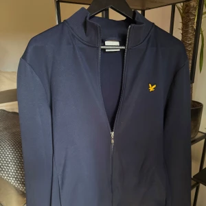 Marinblå full zip-tröja från Lyle & Scott - Riktigt stilren marinblå zip-tröja från Lyle & Scott. Tröjan är nästintill aldrig använd och är i mycket bra skick. Tröjan har hel dragkedja framtill, ribbad krage och är tillverkad i mjuk bomullsmix. Perfekt till lager-på-lager eller bara till casual tillfällen. Ordinarie pris 899kr. 