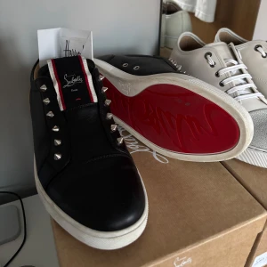 Christian Louboutin sneakers - Svarta sneakers i modellen F.a.v Fique A Vontade från Christian Louboutin i skinn med ikonisk röd sula, silverfärgade nitar längs snörningen och vit yttersula. Snygga detaljer med röd och vit rand på plösen och perforerat innerfoder. Perfekta för dig som vill sticka ut. Storlek 43,5 passar mellan 42,5-44. Og all med kvitto och dustbags, nypris på dessa är ca 10000kr. Skicket är lätt 8,5+ av 10!
