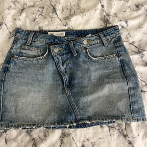 Blå jeanskjol från Zara - Snygg blå jeanskjol från Zara i klassisk femficksmodell. Kjolen har rå kant nertill för en avslappnad vibe och är i en kort modell. Perfekt till sneakers eller boots. Midjehög passform och cool tvättad denim-look. Säljer endast vid bra bud!!