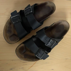 Svarta Birkenstock Arizona  - Fina Birkenstock tofflor/sandaler i storlek 42. Köpta här begagnade men var fel storlek för mig! Dock i mycket fint skick och inte så slitna. Kan hämtas i Tullinge alternativt fraktas om köparen står för frakt-kostnad!