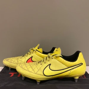 Gula Nike fotbollsskor  - Ett par gamla Nike tempo elit med påse Snygga gula fotbollsskor från Nike i storlek 45. Skorna har klassisk snörning, quiltad ovandel i skinn och metall-dobbar för bästa grepp på planen. Svart Nike-logga på sidan och detaljer i rött. Perfekta för dig som vill sticka ut på matchen.