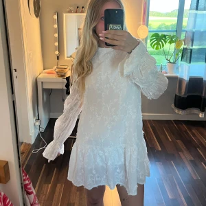 Vit broderad kortklänning med volang - Superfin vit kortklänning med broderade blommor, volang nertill och långa puffiga ärmar. Klänningen har öppen rygg med knytbanda. Perfekt för sommarens alla tillfällen!! Köpt på Nakd för 630kr! Storlek 38 så passar som S/M