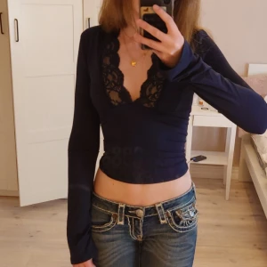 Svart croppad topp med spets - Supersnygg svart croppad topp från Venderbys med lång ärm och djup v-ringning dekorerad med spetsdetaljer. Tight passform som framhäver midjan och ger en trendig look. Min kamera gjorde så den såg mörkblå ut men är egentligen svart! Toppen har aldrig använts