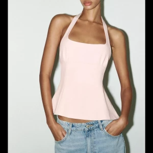 Ljusrosa halterneck topp från Zara - ‼️HELT NY, ALDRIG ANVÄND‼️Supersnygg ljusrosa halterneck topp från Zara med figurnära passform och utsvängd nederdel. Toppen har breda axelband, fyrkantig ringning och två dekorativa band med rosetter i ryggen. Perfekt för dig som vill ha en feminin och trendig look.