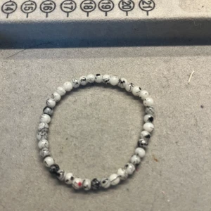 Vitt pärlarmband med svarta detaljer - Stilrent armband med små vita pärlor och svarta marmorliknande detaljer. Pärlorna är trädda på en elastisk tråd vilket gör det enkelt att ta på och av. Perfekt accessoar för att ge din outfit en cool touch. Handgjort!