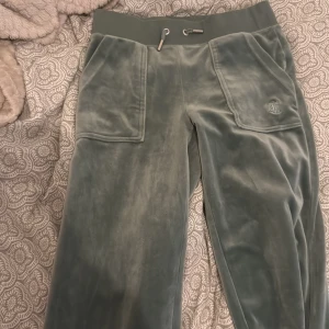 Gröna velourbyxor från Juicy Couture XS - Mysiga gröna mjukisbyxor från Juicy Couture i velour med bred resår i midjan och snörning. Byxorna har stora fickor fram och bak med knappdetaljer och broderad logga på ena fickan. Perfekta för en chill och trendig look. Säljer hela settet för 1900 ❤️