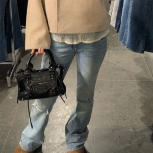 Ljusblå low waist bootcut jeans - Snygga ljusblå jeans med bootcut passform och slitning vid knät. Jeansen har klassisk femficksdesign och är tillverkade i denim. Perfekta för en avslappnad och trendig look.