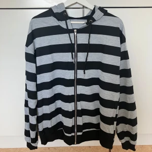 Randig zip-hoodie i svart och grå  - Snygg och mjuk hoodie med dragkedja i klassisk svart- och grårandig design. Perfekt för både vardag och avslappnade helger. Oversized. 209kr på hemsidan. 