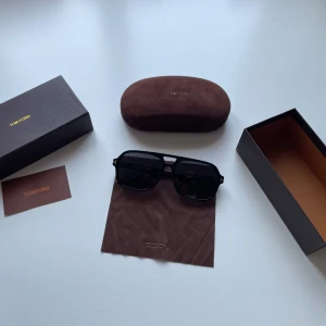 Svarta solglasögon från Tom Ford - Tjena! Säljer ett par snygga svarta solglasögon från Tom Ford med klassisk pilotform och mörka glas. Bågarna är i blank svart plast med guldiga detaljer vid gångjärnen. Kommer med originalfodral och putsduk. Modellen heter Tom ford falconer och passar perfekt nu till sommaren. Tveka inte att skriva vid frågor!