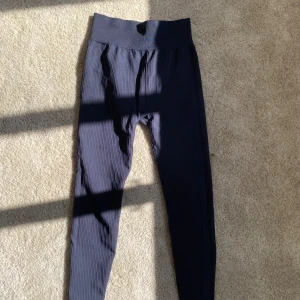 Svarta ribbade leggings från H&M Move - Säljer ett par svarta ribbade leggings från H&M Move i storlek S. De är högmidjade med bred resår i midjan och har en tight passform som sitter snyggt på kroppen. Perfekta för träning eller chill dagar. Materialet är mjukt och stretchigt för maximal komfort.