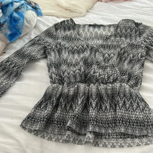 Svartvit blus med mönster och volang - Säljer en svartvit blus med grafiskt mönster och v-ringning. Blusen har långa ärmar och markerad midja med volang nertill som ger en snygg siluett. 