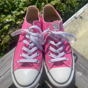 Rosa Converse All Star sneakers - Snygga rosa Converse All Star sneakers i klassisk low-top modell. Skorna har vit gummitå, vita snören och sula med svart rand. Ovandelen är i textil och insidan är ljus. Perfekta för dig som vill sticka ut med färg på fötterna! Andvända en gång. 