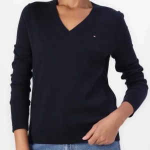 Svart v-ringad tröja Tommy Hilfiger - Klassisk svart v-ringad tröja från Tommy Hilfiger i mjuk pima cotton-blandning. Liten broderad logga på bröstet och långa ärmar. Perfekt till jeans eller kjol för en clean och stilren look.