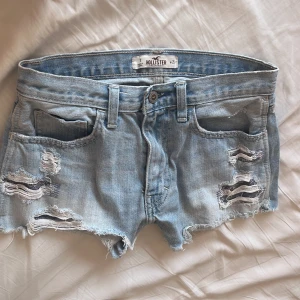 Ljusblå slitna jeansshorts Hollister - Snygga ljusblå jeansshorts från Hollister med slitna detaljer och fransig kant. Klassisk femficksmodell med låg midja och råa kanter för en avslappnad vibe. Perfekta för sommardagar och festivaler.