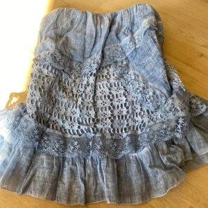 Blå volangkjol med spetsdetaljer - Supersöt blå kortkjol med volanger och broderade spetsdetaljer. Kjolen har ett luftigt tyg och vackra hålmönster som ger en romantisk vibe. Perfekt för dig som gillar boho-stil och vill sticka ut med fina detaljer.