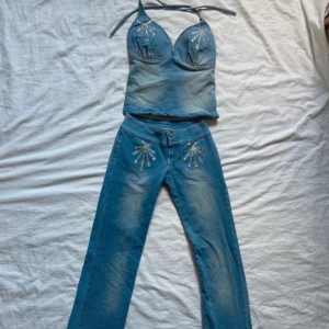 Set - Snygga blå jeansbyxor med raka ben och coola strassdetaljer vid fickorna framtill. Byxorna har en klassisk femficksmodell och stängs med knapp och dragkedja. Perfekta för dig som vill sticka ut lite extra.