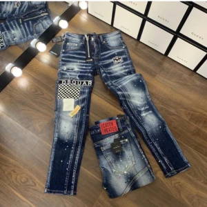 Dsquared2 blå jeans  - Snygga blå jeans från Dsquared2 med slitningar, patchar och coola detaljer som checker-mönster och broderade märken. Jeansen har smal passform, normal midja och färgstänk för en edgy look. Perfekta för dig som vill sticka ut.