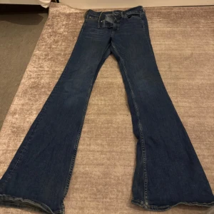 Blå bootcut jeans från &Denim - Snygga blå bootcut jeans från &Denim med klassisk femficksmodell och normalhög midja. Jeansen har breda utsvängda ben och är tillverkade i ett mjukt denimtyg. Perfekta för dig som gillar retrovibbar och vill ha en cool siluett.