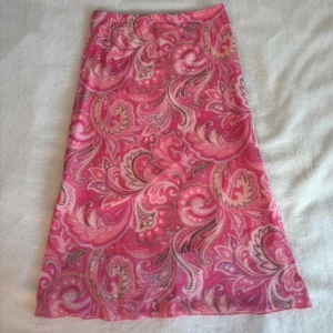 Rosa midi kjol  - Superfin långkjol i olika rosa nyanser med paisleyinspirerat mönster. Kjolen har en lätt utsvängd form och känns riktigt somrig och färgglad. Perfekt för dig som vill sticka ut med en unik och lekfull stil.