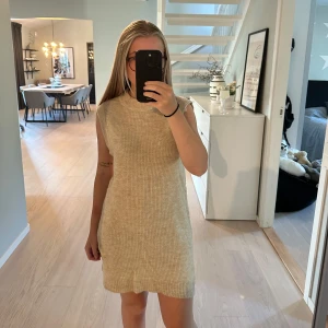 Beige stickad ärmlös klänning - Supermysig beige stickad klänning i kort modell. Ärmlös med rund halsringning och ribbad struktur. Perfekt att styla med boots eller sneakers för en chill look. Liten slits på sidan ger extra vibe. Aldrig använd/utan prislapp