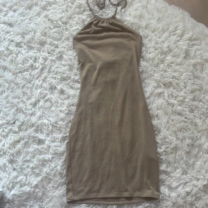 Beige kort klänning från H&M Divided - Supersnygg beige kort klänning från H&M Divided i storlek XXS. Klänningen har halterneck med knytband och är ärmlös. Den är figurnära och gjord i ett mjukt bomullsmaterial, perfekt för varma dagar.