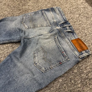 Replay Anbass ljusblå jeans (Krobbes) - Säljer ett par Replay Anbass jeans i ljusblå tvätt med snygga slitningar och klassiska femficksdetaljer. Jeansen har raka ben, normal passform och läderpatch med Replay-logga bak. Perfekta för dig som gillar en avslappnad men stilren look. Fint skick! 499kr + frakt. Välmött, BB🍾