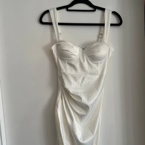 Vit satin kortklänning med slits - Supersnygg vit kortklänning i satin med breda axelband, markerad byst och draperad detalj framtill. Klänningen har en hög slits och figurnära passform som ger en riktigt chic look. Använd en gång, nyfris 1000