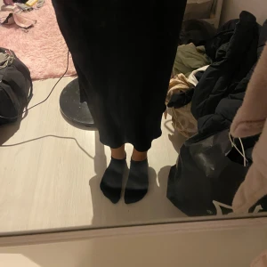 Svart långkjol från Amisu, stl 34 - En stilren svart långkjol från Amisu i storlek 34. Kjolen har en rak och enkel passform som ger en clean look. Det är ett glansigt master som känns mjukt och följsamt mot huden. Perfekt för dig som gillar minimalistisk stil och vill ha en kjol som funkar till många olika outfits. Den har även en dragkedja uppe på sidan så den är lätt att komma i. 