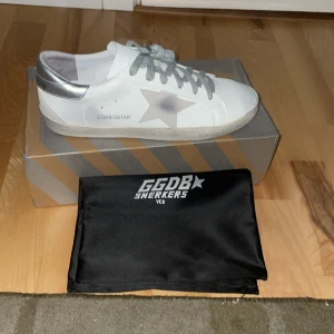 Golden Goose Superstar sneakers silver/vit - Golden Goose Superstar sneakers  med silverfärgade detaljer och grå snörning. Klassisk stjärndesign på sidan och logga på hälen.  platt sula och rund tå. 