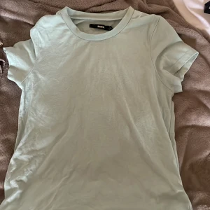 Ljusblå basic t-shirt från Bik Bok - Enkel och fräsch ljusblå t-shirt från Bik Bok i storlek XS. T-shirten har klassisk rund halsringning och korta ärmar. Perfekt för en clean och avslappnad stil. Materialet känns mjukt och skönt mot huden.