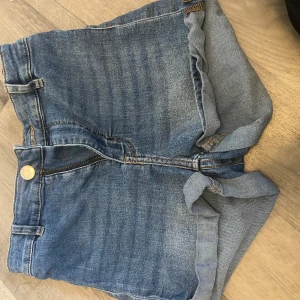 Blå jeansshorts - Snygga blå jeansshorts i klassisk denim med uppvikta benslut. Shortsen har normal passform, gylf med dragkedja och knapp samt bälteshällor. Perfekta för varma sommardagar och enkel att matcha med allt.