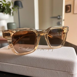 Beige transparenta solglasögon CHIMI - Snygga solglasögon från CHIMI med transparent beige båge och bruna glas. Rektangulär form med coola detaljer på skalmarna och diskret CHIMI-logga. Perfekta för att lyfta din stil med en modern touch. Inga repor 