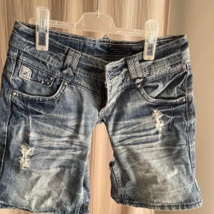 Blå slitna jeansshorts från West Made - (Väldigt low waist för mig) Riktigt snygga blå jeansshorts från West Made med slitna detaljer och coola rivna partier. Klassisk femficksmodell, låg midja och dragkedja framtill. Perfekta för en avslappnad streetstil under sommaren.