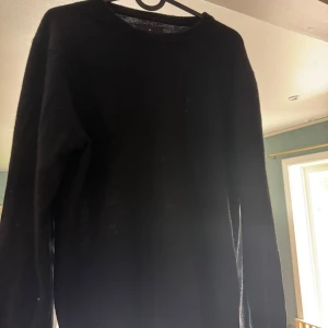 Svart stickad tröja från Wagner - En svart stickad tröja från Wagner  med rund halsringning och långa ärmar. Tröjan har en enkel och clean look med en liten diskret kronlogga. Perfekt för dig som gillar minimalistisk stil och vill ha något som funkar till många outfits.