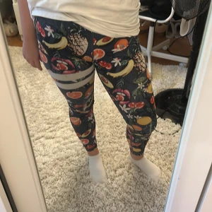 Färgglada leggings från Stronger S - Säljer ett par snygga leggings från Stronger i storlek S. De är mörkblå med ett färgstarkt fruktmönster med ananas, apelsin, avokado och blommor. Materialet är stretchigt och består av 85% polyester och 15% elastan. Perfekta för träning eller chill. Har även en mobilficka!
