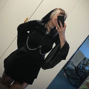 Svart sammetklänning med snörning från Killstar - Säljer en svart långärmad klänning i sammet från Killstar. Klänningen har snörning framtill vid halsen, vida ärmar och en djup huva baktill.