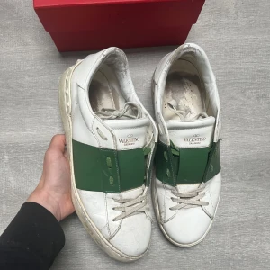 Valentino Garavani Open sneakers vit/grön - Snygga Valentino Garavani Open sneakers i vitt skinn med bred grön läderdetalj över mitten och matchande gröna skosnören. Klassisk rund tå och platt sula, perfekt för dig som gillar exklusiva och trendiga sneakers med unik design. Priset är ej hugget i sten!
