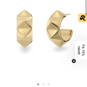 Chunky guldiga örhängen med pyramidmönster - Säljer ett par chunky örhängen i guld med coolt pyramidformat mönster. De är halvbågsformade och har en riktigt snygg, glansig finish som sticker ut. Perfekta för dig som vill ha ett statement-smycke med edgy vibe. ifrån edblad
