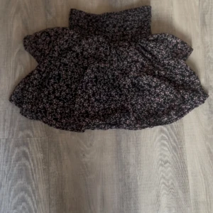 Svart blommig kortkjol från Kappahl - Supersöt svart kortkjol från Kappahl med små ljusrosa blommor. Kjolen har smock i midjan för en bekväm passform och ett flowigt fall. Perfekt för dig som gillar romantiska och feminina vibes.