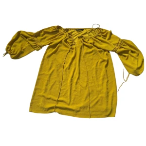 Gul kortklänning från Trafaluc - Snygg gul kortklänning från Trafaluc med trekvartsärmar och resår vid halsringningen. Klänningen har en avslappnad passform och knytband vid halsen för en cool touch. Perfekt för dig som gillar färg och vill sticka ut lite extra.