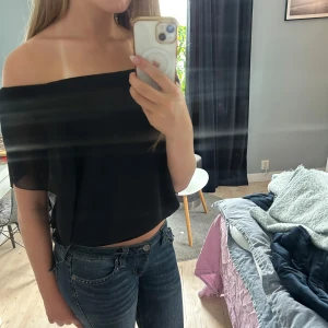 Svart offshoulder topp i chiffong - Säljer en svart offshoulder topp med lös passform och bred resår nertill. Toppen är ärmlös och har en luftig, flowy känsla tack vare det tunna materialet. Perfekt för dig som gillar en stilren och enkel look med lite edge.
