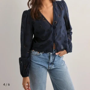 Mörkblå blus med knyt och broderi - Säljer en mörkblå blus med v-ringning och knyt framtill. Blusen har långa ärmar med lätt puff och fina broderade blommor som ger en cool och romantisk vibe. Perfekt till jeans eller kjol för en trendig look. Prislappen är kvar!!