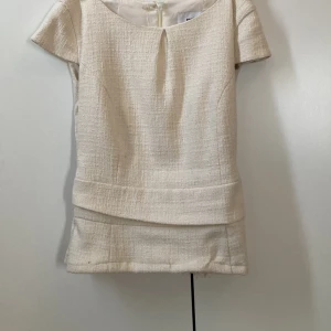 Beige blus från Ströms Stockholm - Snygg beige blus från Ströms Stockholm i strukturerat tyg med korta ärmar och rund halsringning. Blusen har en markerad midja och dragkedja bak för enkel påklädning. Perfekt för dig som gillar stilrena och klassiska plagg med en twist. Sydd av en gammal klänning!