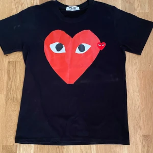 Svart Comme des Garçons Play t-shirt - Svart t-shirt från Comme des Garçons Play med stort rött hjärta med ögon tryckt på bröstet och ett mindre hjärta bredvid. Klassisk rund hals och korta ärmar. Ikonisk och stilren design som sticker ut. Tillverkad i mjuk bomull för skön känsla.